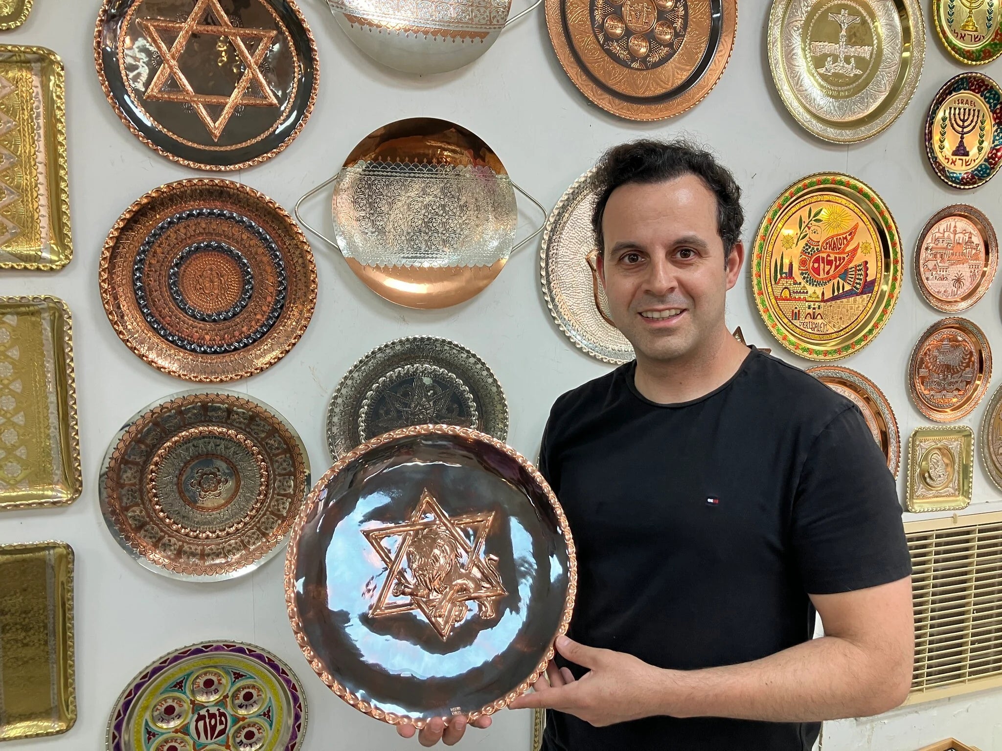 Miro family coppersmith holding a handcrafted copper Star of David plate in the Akko workshop